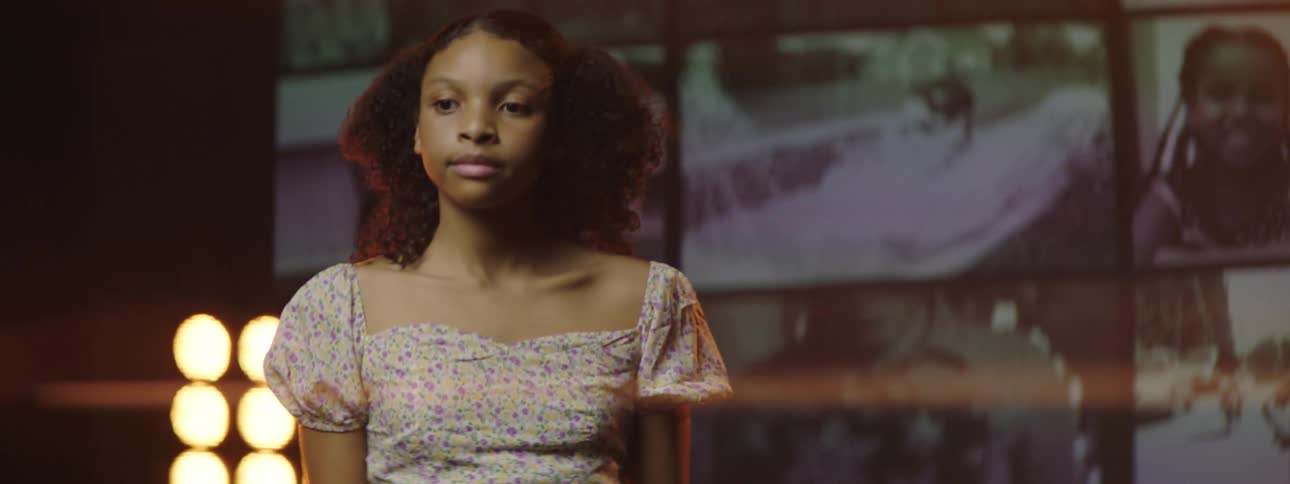 Black teenager turns her head away from the screens behind her