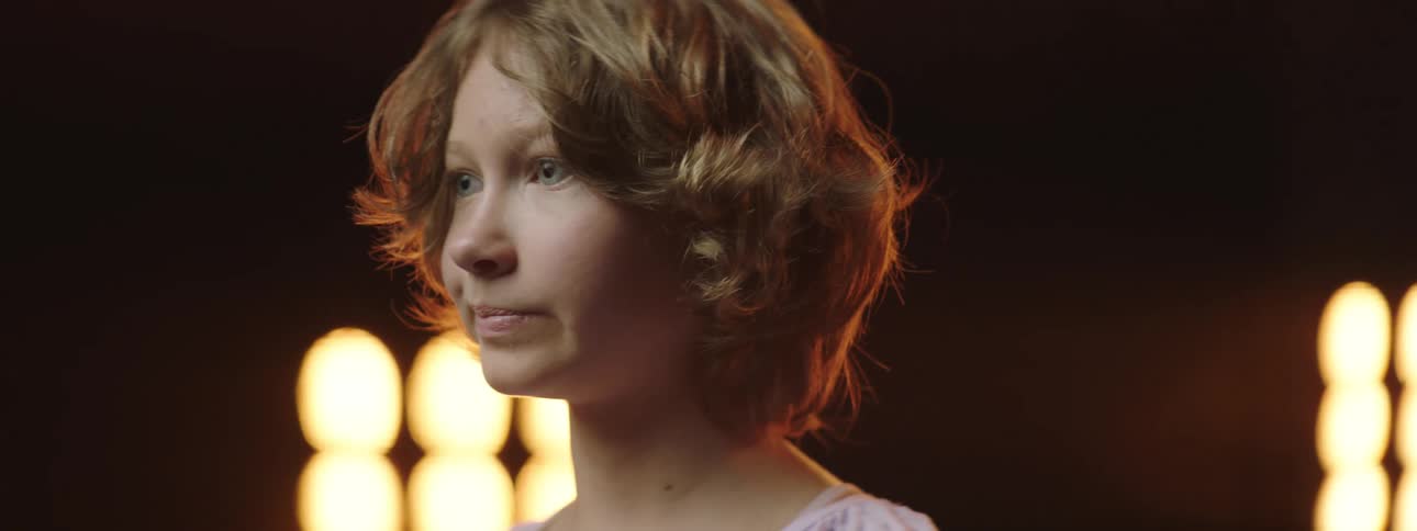 Teenaged girl turns her head as she stands in front of some bright lights