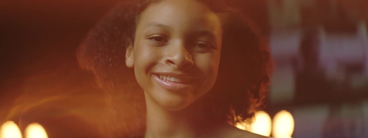 A smiling girl turns her head while stage lights glow and glare