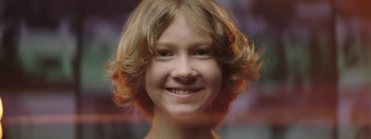 A child goes from serious to smiling with video playing on a wall of screens behind him