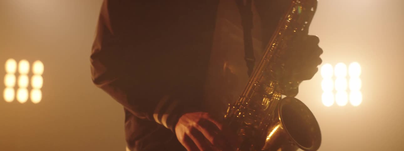 Saxophone player plays standing on foggy stage under bright stage lights