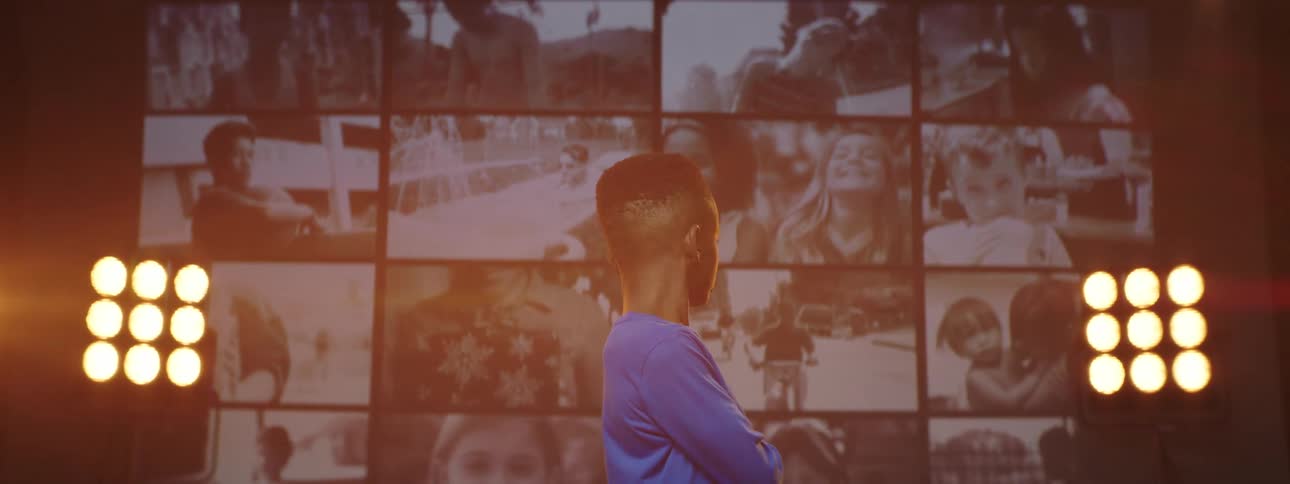 A young boy stands on a stage looking behind him at the large screens