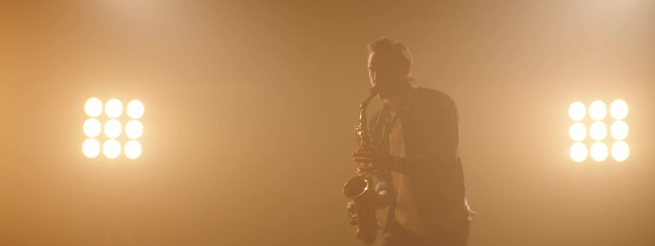 A saxophonist plays the saxophone in front of large light arrays on stage
