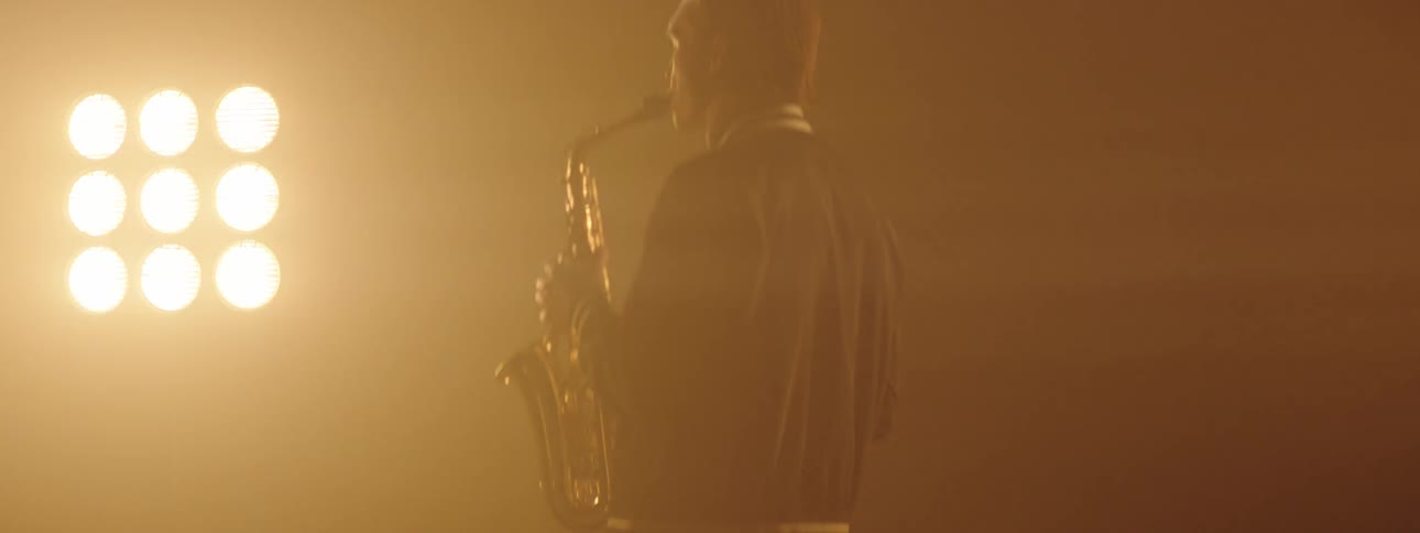 A man plays the saxophone while stage lights glow behind him