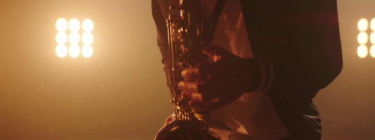 Man plays a saxophone with bright lights shining behind him