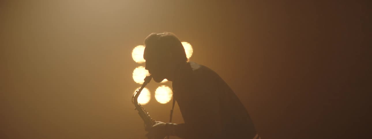Silhouette of a man playing saxophone on a smoky stage under yellow lights