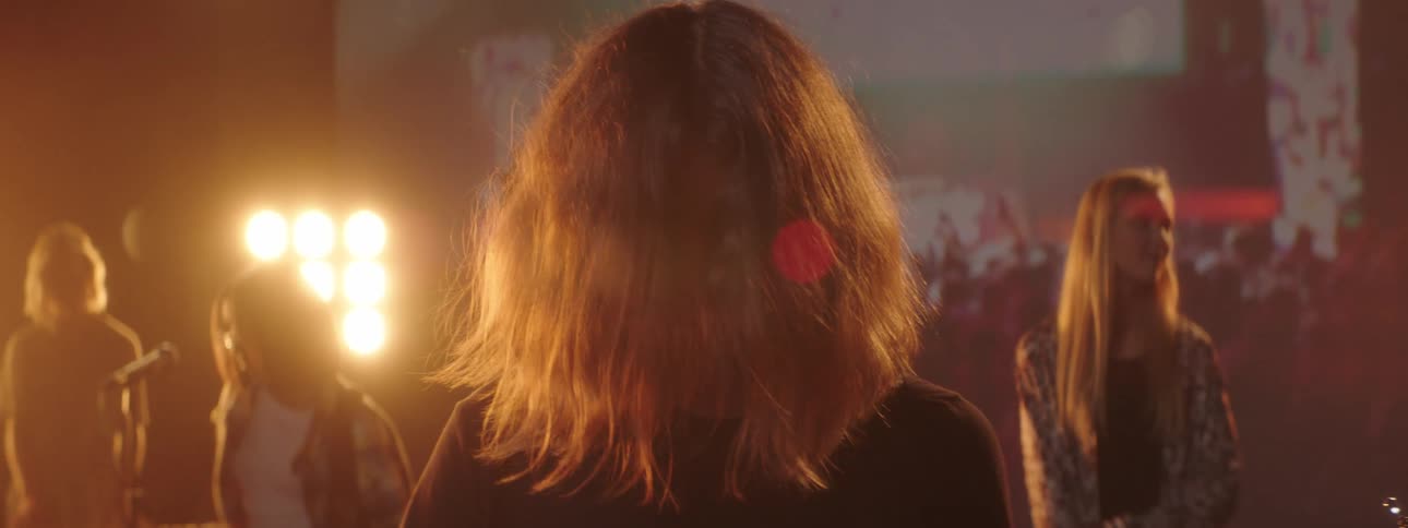 One guitarist playing on stage backed by digital screens among others through her hair back