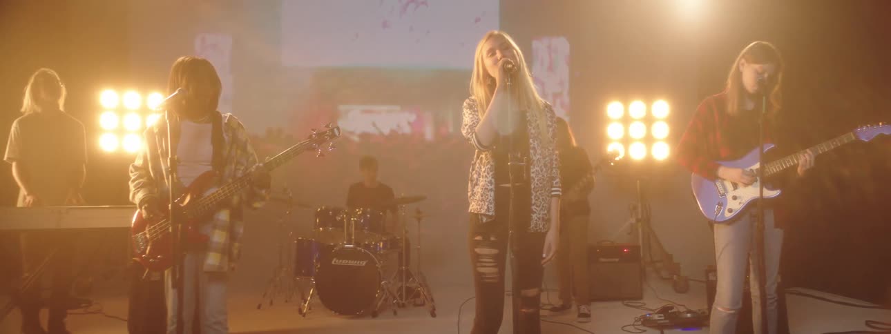 Women and a man in a band perform on a stage