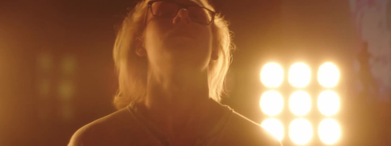Man with long blonde hair and glasses plays electronic keyboard in bar