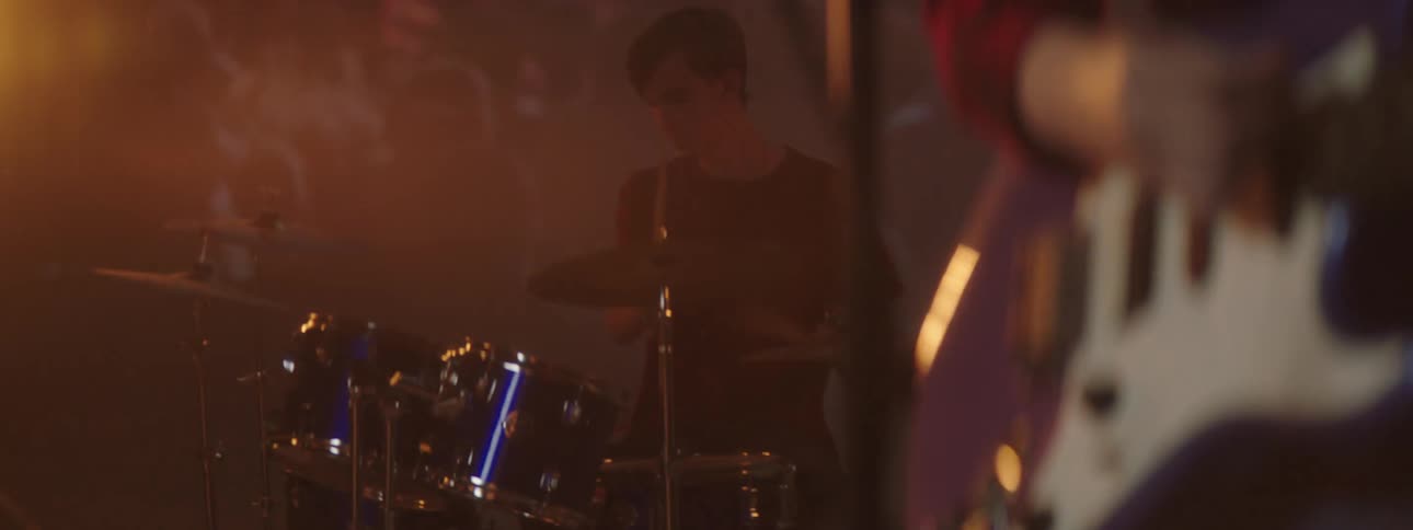 Two people play drums and guitar on a foggy stage