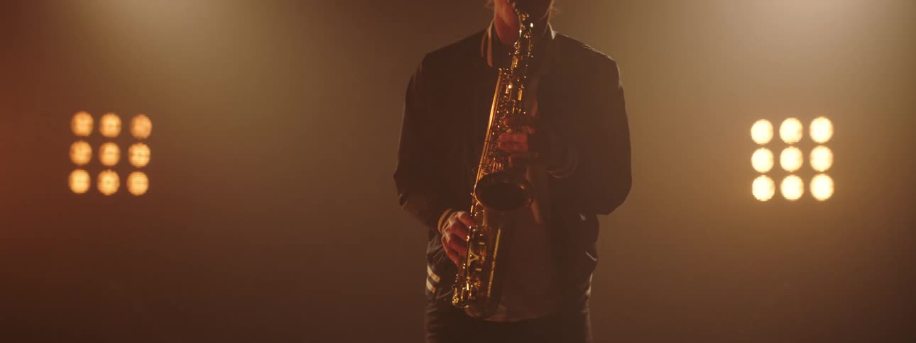 A man plays the saxophone in front of a grid of lights