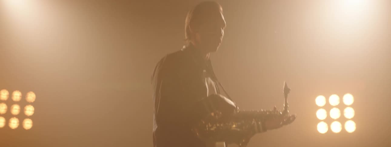 Man holds a saxophone as he dances under the bright lights
