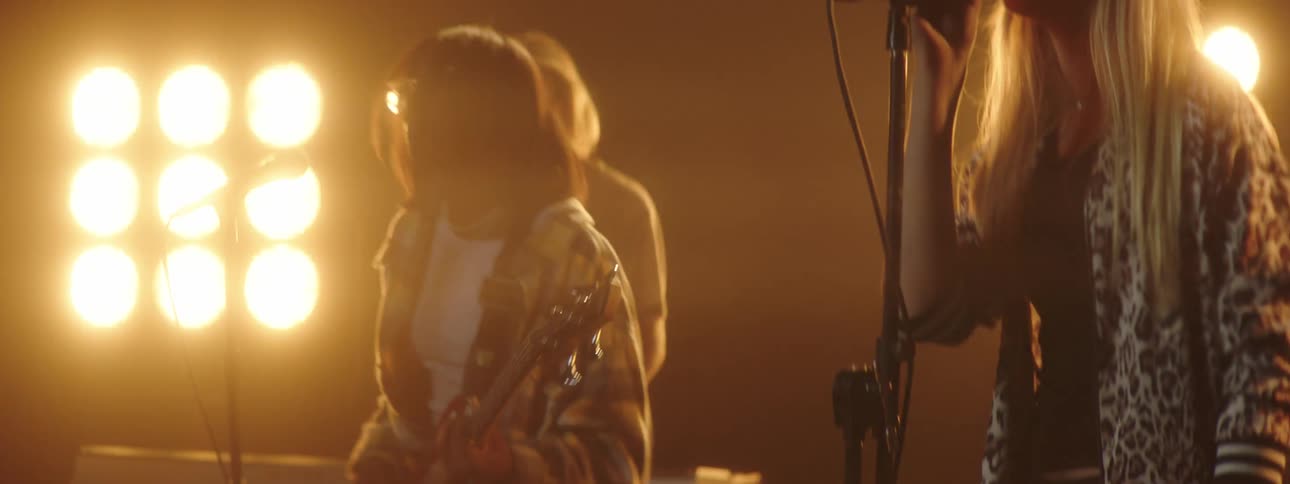 A girl sings with her band as they perform in front of a screen playing video of a concert