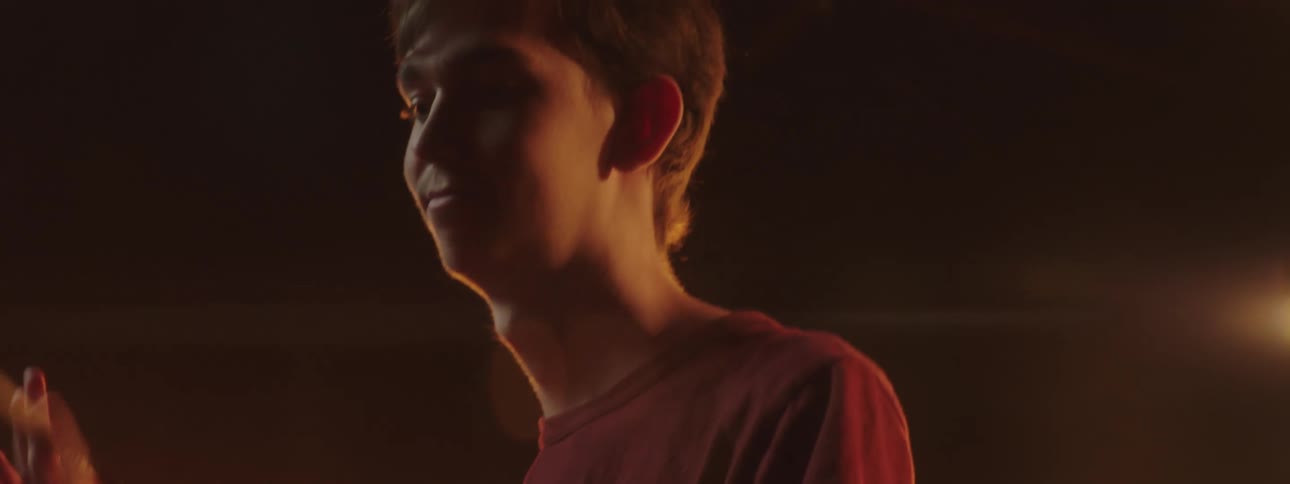 A boy twirls a drumstick in his hand standing on stage with lights shining behind him