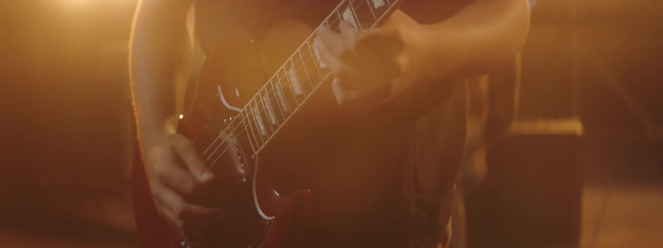 A teenager in a band plays guitar on stage with lights shining and glaring
