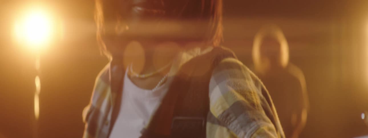 Black woman plays an electric guitar as bright lights shine from behind her