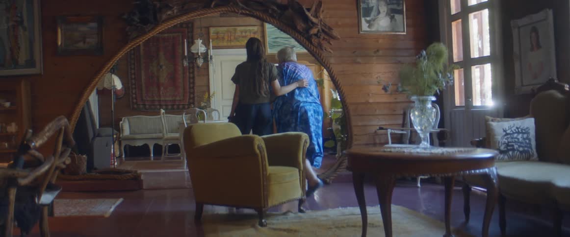 A young woman assists an elderly woman walking across the room
