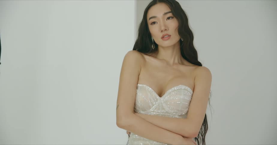 Female model with wavy hair and white dress poses for the camera in the studio