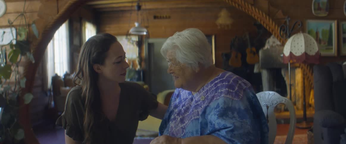 A woman strokes the shoulder of an older woman as they talk with one another at a table
