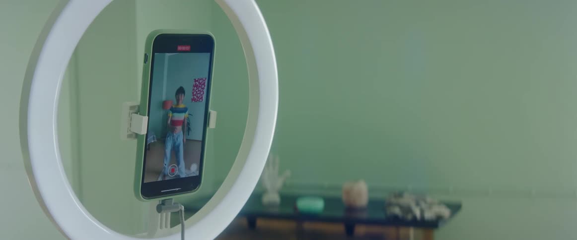 A phone stand holds a smartphone recording a woman dancing in her room
