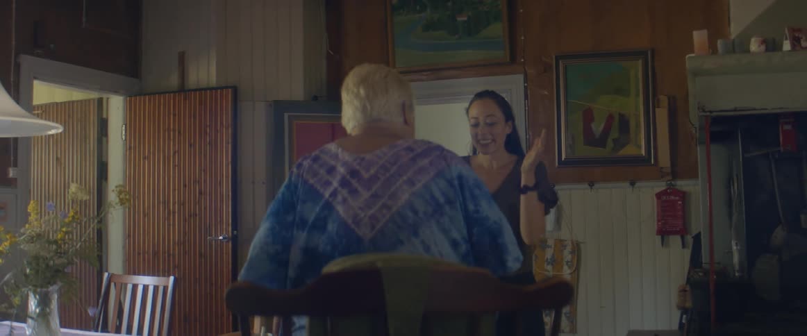 An elderly woman stands from her chair to hug and greet her granddaughter