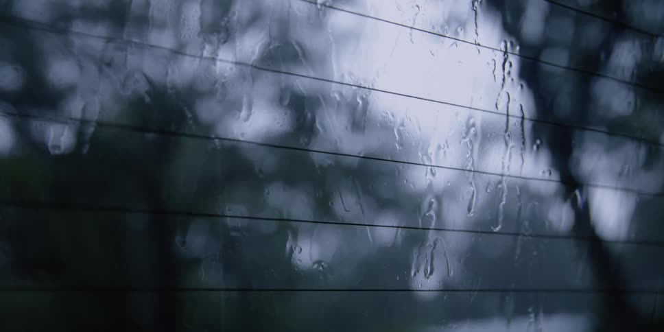 Rain water streams down the rear window of a vehicle during light rainy weather