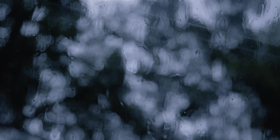 A window with raindrops with trees the sky and clouds in the background