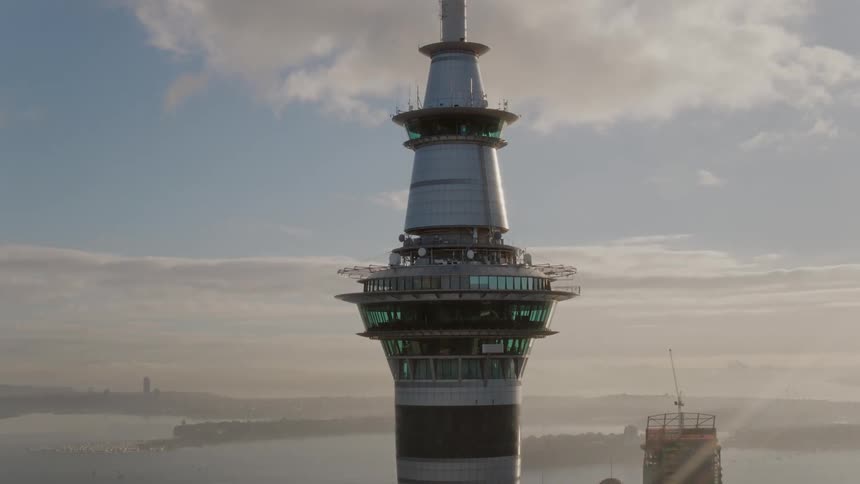 Tower with observation platforms stands near marina and water as traffic flows along street