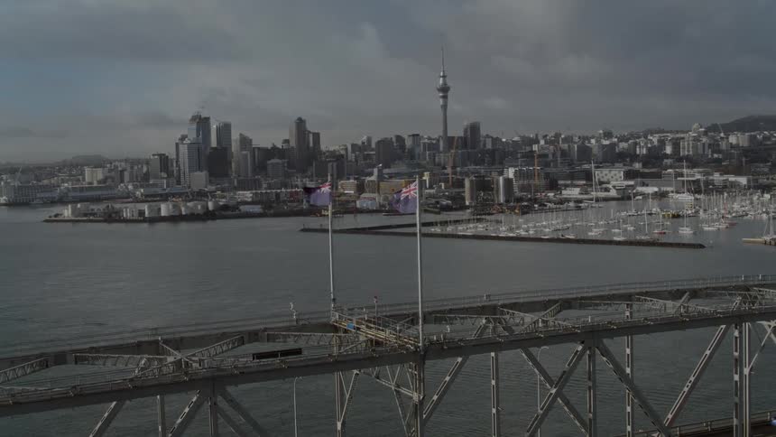 A bridge with two flags with a river a city skyline the sky and clouds in the background