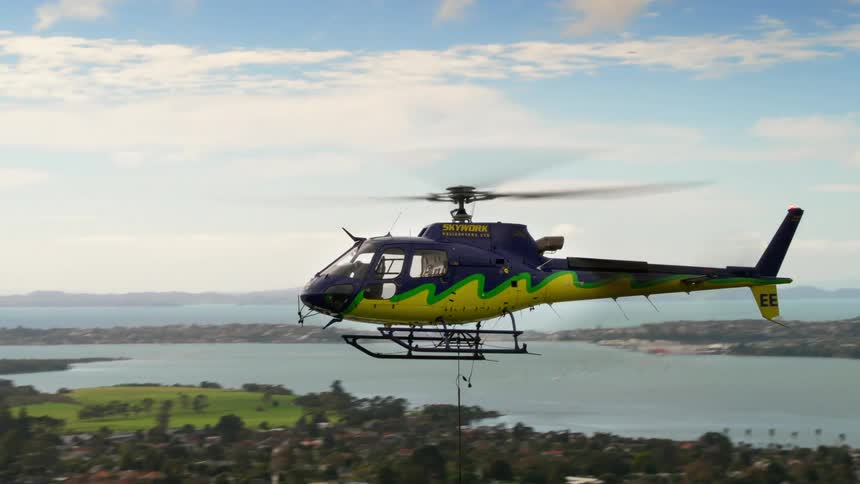 A helicopter flies lower to the ground as it moves from over the ocean to a neighborhood