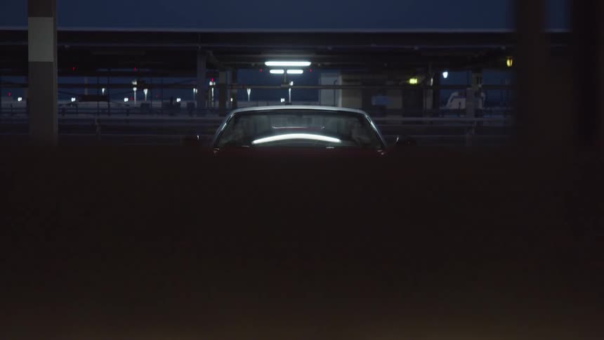 A red convertible sits with headlights on in a parking garage