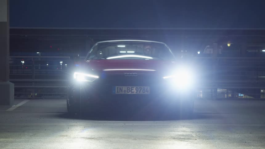 Man sitting in red car turning on headlights