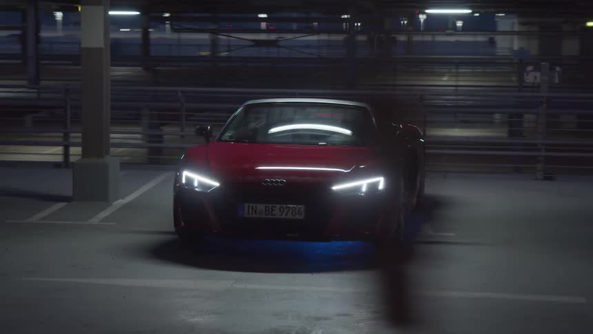 A sports car with headlights in a garage with signs and lights in the background