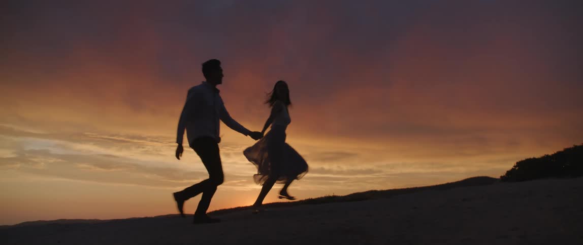 A man and a woman holding hands and walking with the sky and clouds in the background