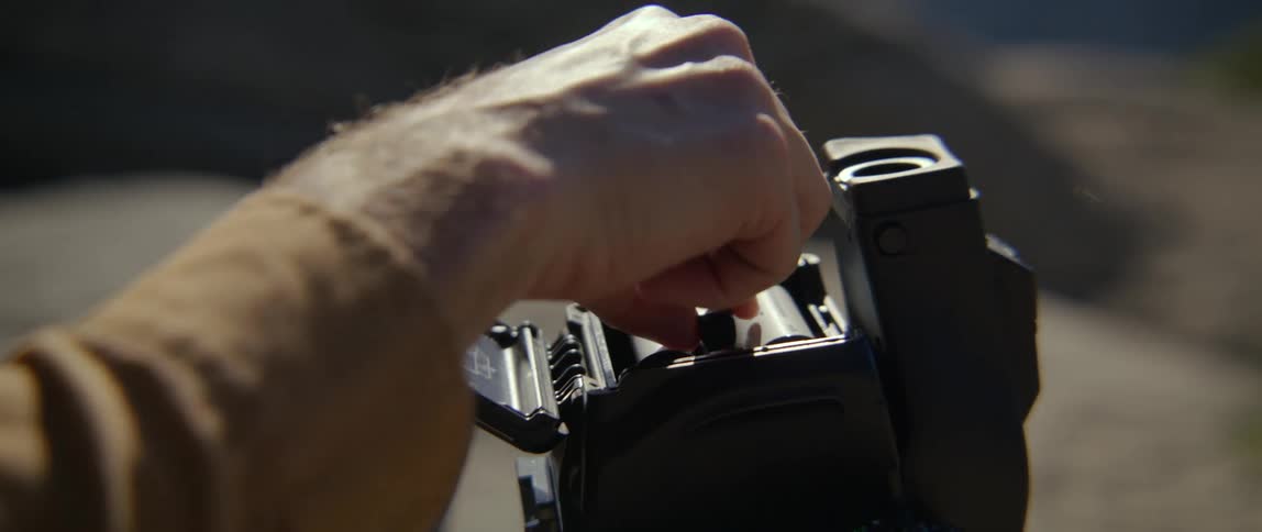 A man puts film in a camera while resting in a canyon