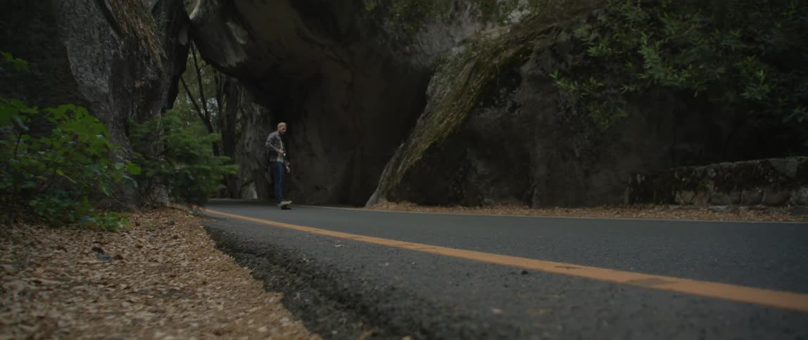 A man riding a skateboard on a road with a cliff and trees in the background