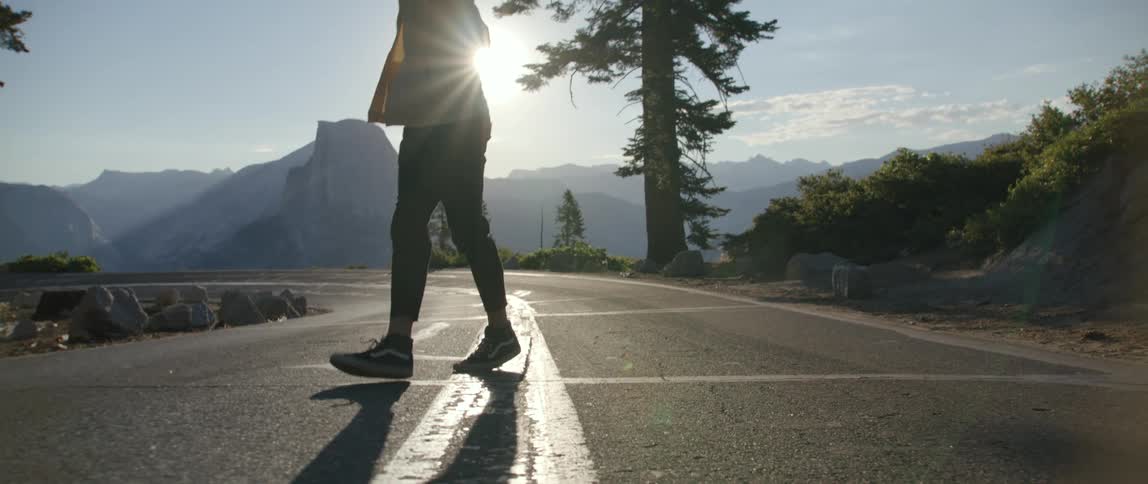A man walks down a deserted road in the mountains turning around to see the sunrise