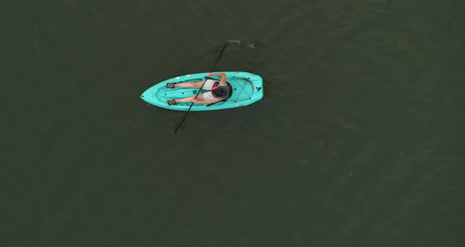 A person uses an oar to paddle in a kayak along a lake