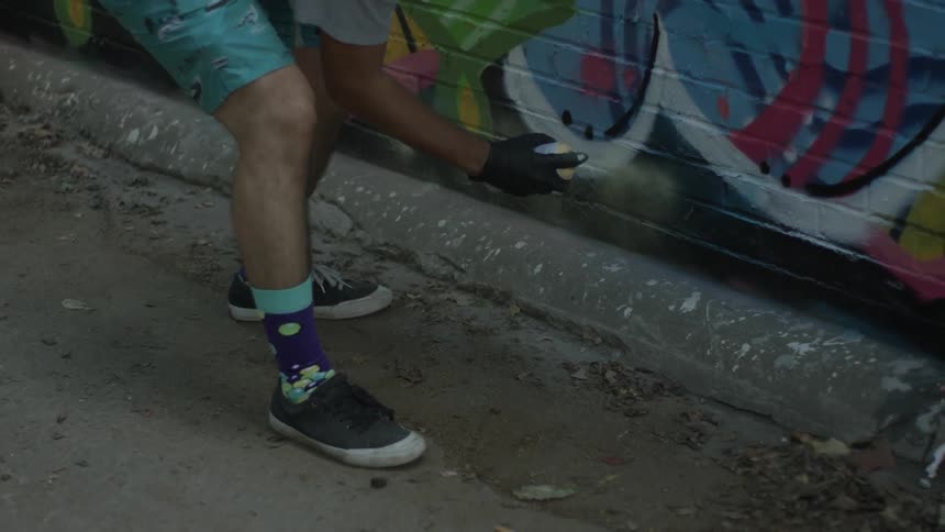 A man is crouched as he spray paints a wall