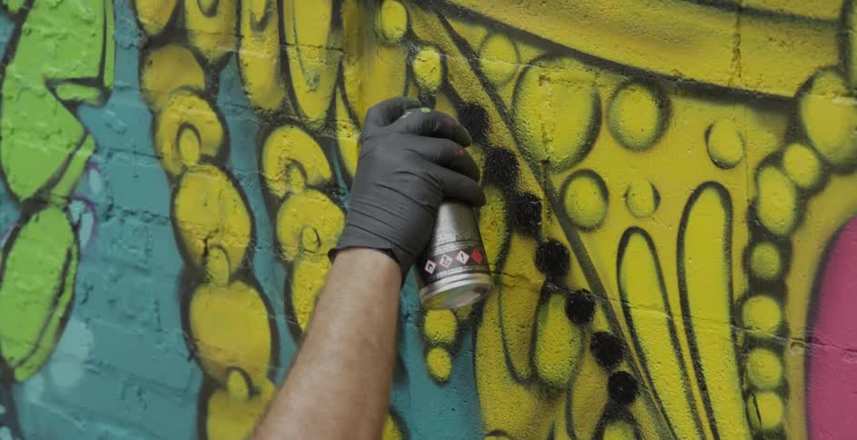 A person is spray painting black dots on a brick wall
