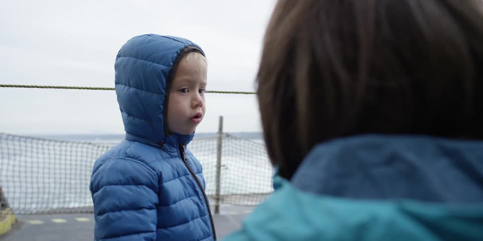 A boy in a puffy blue jacket talks to a woman