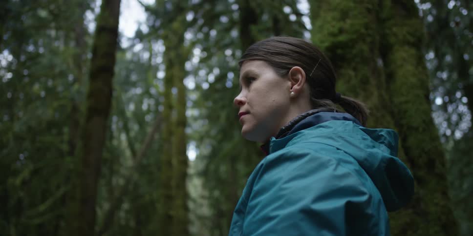 A woman stands in a forest before walking forward