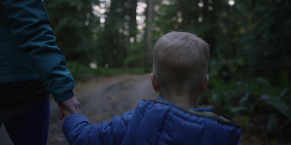 A mom and her child walking down a dim forest path