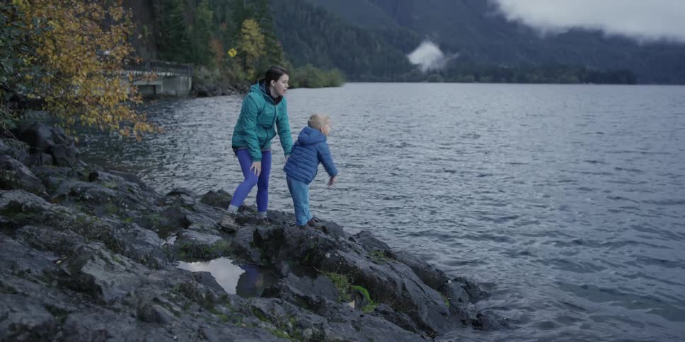 A mother watches her child as he throws a rock into the water