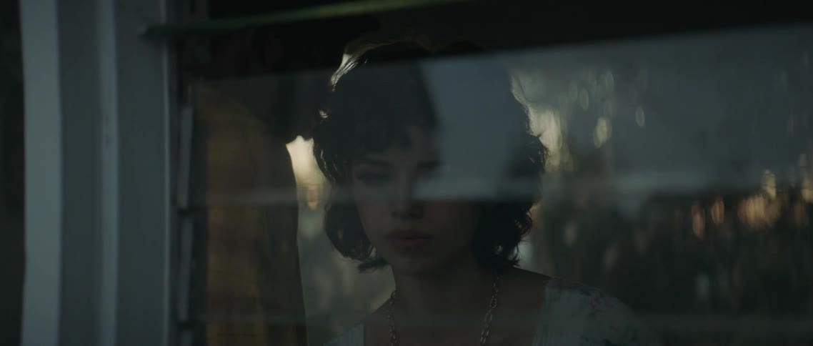 A young woman and be seen from outside as she looks pensively out a window