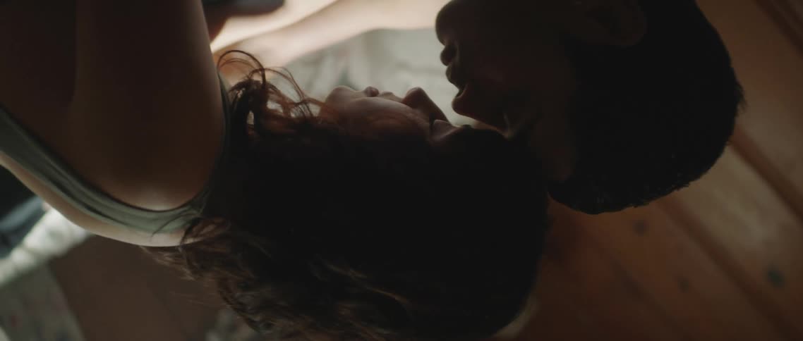 Couple sit together on bed leaning their foreheads together