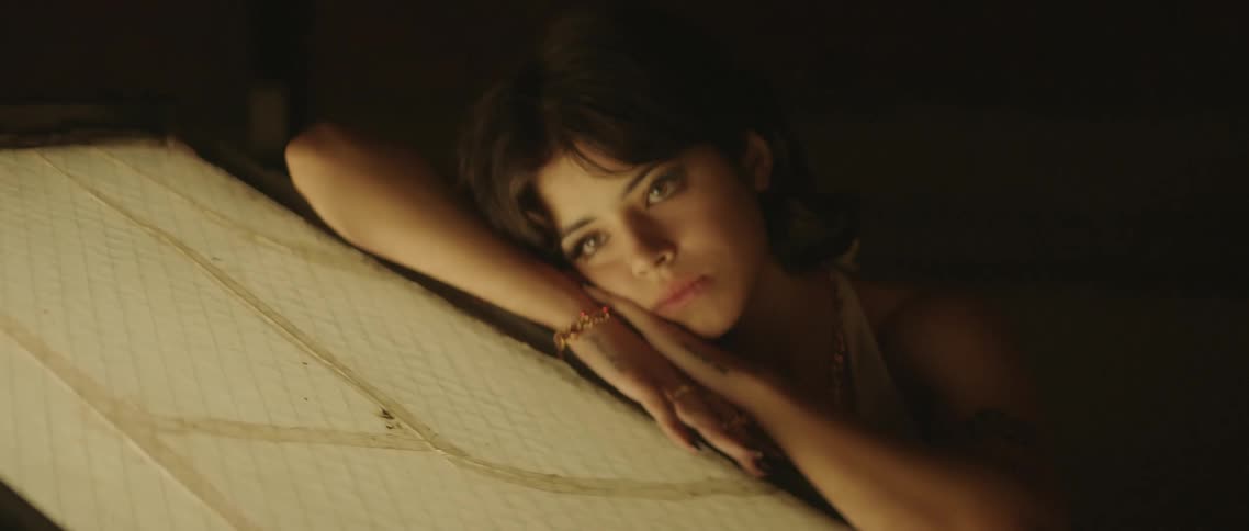 A young woman rests against a skylight on a rooftop at night