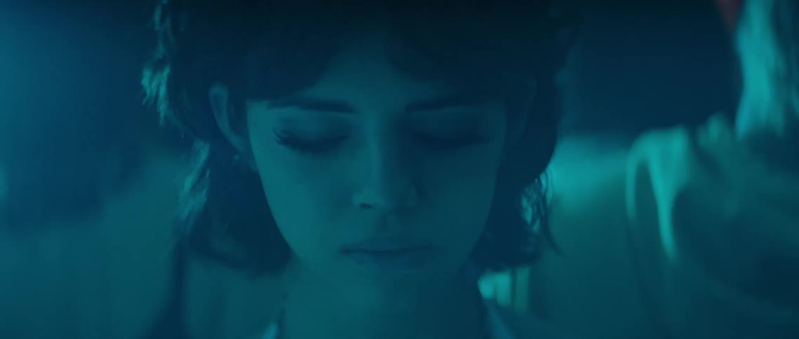 A woman stands amidst many party goers in a dark room as she looks up at the camera