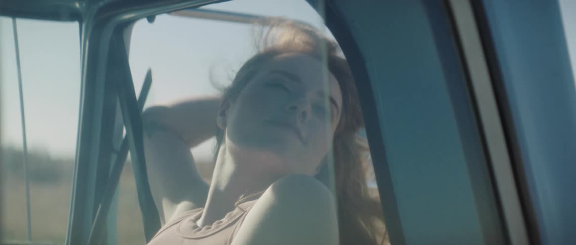 A woman is travelling in a car as she tilts her head slightly outside the window