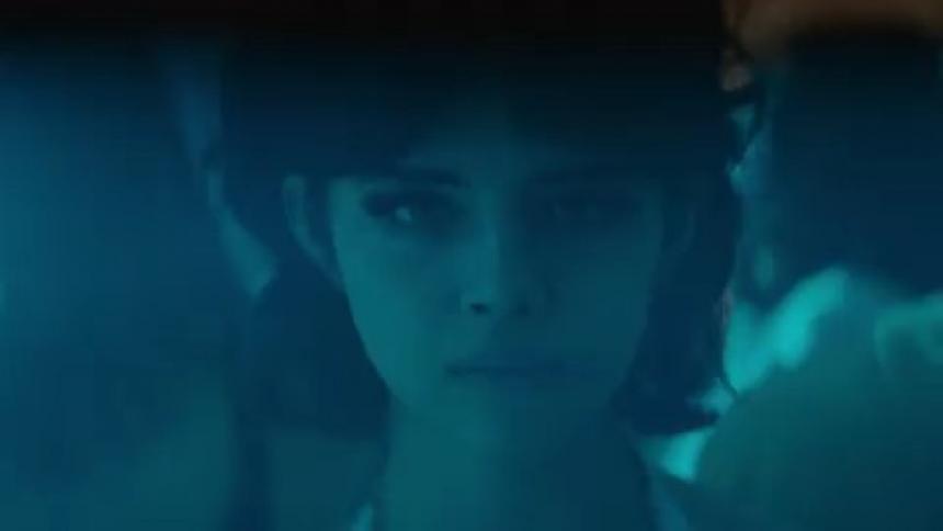 A woman is standing still as people dance at a party